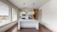 This single-floor residence is thoughtfully designed with a neutral, contemporary palette and a cohesive blend of materials throughout. The kitchen serves as a central highlight, featuring white cabinetry, subway tile backsplash, stainless steel appliances — including a French door refrigerator, range, and built-in microwave — and a generously sized island with a white quartz countertop and undermount sink. Pendant lighting with antique brass fixtures adds warmth, while multiple windows allow ample natural light to fill the space. Rich, dark-toned hardwood flooring extends throughout the main living areas, lending a sense of warmth and continuity.

The bedrooms are carpeted and bright, each equipped with a ceiling fan and windows that bring in natural light. Closet space is well-considered, with at least one walk-in closet featuring built-in shelving and rod storage.

Two full bathrooms maintain a consistent design language, each offering a tub-shower combination with tile surround, a wide vanity with white cabinetry and brushed hardware, and large-format tile flooring. A well-lit hallway with panel-style doors connects the rooms, creating a smooth and functional flow throughout the residence.