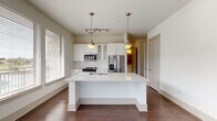 This single-floor residence is thoughtfully designed with a neutral, contemporary palette and a cohesive blend of materials throughout. The kitchen serves as a central highlight, featuring white cabinetry, subway tile backsplash, stainless steel appliances — including a French door refrigerator, range, and built-in microwave — and a generously sized island with a white quartz countertop and undermount sink. Pendant lighting with antique brass fixtures adds warmth, while multiple windows allow ample natural light to fill the space. Rich, dark-toned hardwood flooring extends throughout the main living areas, lending a sense of warmth and continuity.

The bedrooms are carpeted and bright, each equipped with a ceiling fan and windows that bring in natural light. Closet space is well-considered, with at least one walk-in closet featuring built-in shelving and rod storage.

Two full bathrooms maintain a consistent design language, each offering a tub-shower combination with tile surround, a wide vanity with white cabinetry and brushed hardware, and large-format tile flooring. A well-lit hallway with panel-style doors connects the rooms, creating a smooth and functional flow throughout the residence.