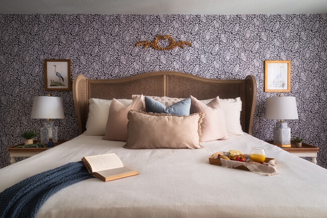 Un dormitorio elegante con cabecero de ratán, almohadas acogedoras y una pared decorativa estampada. - 715 Grandin Rd