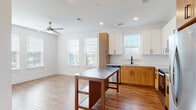 Located at 1290 Old Peachtree Rd NW in Duluth, Georgia, this single-floor residence presents a clean, contemporary design with a cohesive neutral palette and warm wood-toned accents throughout. Hardwood-style flooring flows through the main living areas and hallways, complemented by crisp white walls and recessed lighting that create a bright, welcoming atmosphere.

The kitchen is a standout feature, showcasing a two-tone cabinetry design that pairs white upper cabinets with warm wood lower cabinets, set against a classic white subway tile backsplash. Granite countertops, stainless steel appliances — including a range and built-in microwave — and a deep undermount sink complete the space. A mobile kitchen island with a stainless steel top provides additional workspace and flexibility. Multiple windows allow natural light to fill the kitchen and adjoining living area, which is equipped with a ceiling fan.

The primary bedroom offers plush carpeting, a ceiling fan, and direct access to a generous walk-in closet with wire shelving systems. The primary bathroom features a dual-sink vanity with granite countertops, wood cabinetry with matte black hardware, and a separate shower. A secondary bathroom includes a single vanity with granite countertop and a tub-shower combination. A well-proportioned entry hallway with recessed lighting completes this thoughtfully designed residence.