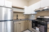 Located at 200 Godwin Ave in Paterson, NJ, this thoughtfully designed single-floor unit showcases a clean, modern aesthetic throughout. The living areas feature light wood-tone flooring that runs seamlessly across the space, complemented by crisp white walls and bright white baseboards that lend a fresh, airy feel. Large black-framed windows invite generous amounts of natural light and offer pleasant views of surrounding greenery, enhancing the open and welcoming ambiance of the living and bedroom spaces. The bedrooms are well-proportioned, with one featuring dual windows for added brightness and another with convenient built-in closet storage complete with shelving. The kitchen is outfitted with two-tone cabinetry — upper white cabinets paired with lower wood-grain units — set against a contemporary rectangular tile backsplash. A stainless steel gas range with an overhead ventilation hood anchors the cooking space, while grey countertops and large-format floor tiles complete the functional, modern look. The bathroom offers an elegant contrast of dark grey marble-look wall tiles alongside white marble-patterned floor tiles, housing a full soaking tub with shower and a modern white toilet. The overall layout, as reflected in the floor plan, is efficiently organized, offering a well-connected flow between all areas of the home.