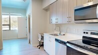 Located at 300 Massachusetts Ave in Amherst, Massachusetts, this efficiently designed single-floor studio offers a thoughtful layout that maximizes every square foot of its compact footprint. The interior features a clean, contemporary aesthetic throughout, with light wood-tone finishes, crisp white surfaces, and smooth light-toned flooring that lends a bright, cohesive feel to the entire space.

The galley-style kitchen is well-appointed with a full suite of stainless steel appliances, including an electric range, over-the-range microwave, dishwasher, and refrigerator. Light wood cabinetry extends to the ceiling, providing generous storage, while white quartz countertops offer a sleek, functional workspace. A built-in desk area is seamlessly integrated into the kitchen corridor, making efficient use of the available space.

The sleeping area accommodates a full-sized bed and includes a dedicated study nook positioned beside a window that allows natural light to filter in. An in-unit washer is also present, adding everyday convenience.

The bathroom features a modern vanity with light wood cabinetry, a white countertop, and a large mirror, maintaining the same refined design language found throughout the unit. The open sightlines between rooms contribute to an airy atmosphere, making this a practical and stylishly appointed living space.