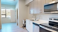 Located at 300 Massachusetts Ave in Amherst, Massachusetts, this efficiently designed single-floor studio offers a thoughtful layout that maximizes every square foot of its compact footprint. The interior features a clean, contemporary aesthetic throughout, with light wood-tone finishes, crisp white surfaces, and smooth light-toned flooring that lends a bright, cohesive feel to the entire space.

The galley-style kitchen is well-appointed with a full suite of stainless steel appliances, including an electric range, over-the-range microwave, dishwasher, and refrigerator. Light wood cabinetry extends to the ceiling, providing generous storage, while white quartz countertops offer a sleek, functional workspace. A built-in desk area is seamlessly integrated into the kitchen corridor, making efficient use of the available space.

The sleeping area accommodates a full-sized bed and includes a dedicated study nook positioned beside a window that allows natural light to filter in. An in-unit washer is also present, adding everyday convenience.

The bathroom features a modern vanity with light wood cabinetry, a white countertop, and a large mirror, maintaining the same refined design language found throughout the unit. The open sightlines between rooms contribute to an airy atmosphere, making this a practical and stylishly appointed living space.