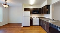 This two-floor residence offers a practical and comfortable layout designed for everyday living. The kitchen serves as a central hub on the main floor, featuring dark espresso cabinetry with granite-style countertops, a gas range, built-in microwave, full-size refrigerator, and a dishwasher. A peninsula counter connects the kitchen to the adjacent dining and living areas, creating an open, communicative flow between spaces. The living room is carpeted and benefits from a ceiling fan and a large sliding glass door that invites an abundance of natural light and provides views of the lush greenery outside. Track lighting adds a modern touch to the space. The main floor also includes a staircase with a decorative iron railing leading to the upper level. Upstairs, the bedrooms are carpeted and each equipped with ceiling fans. The primary bedroom features multiple windows for natural light and a spacious closet with sliding doors and built-in shelving. The bathrooms are well-sized, featuring wide vanity counters with integrated sinks, large mirrors, and shower-tub combinations. Throughout the home, warm hardwood-style flooring in the kitchen and neutral carpet tones in the living and sleeping areas create a cohesive and inviting atmosphere.