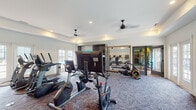 Located at 11107 Conductor Cir in Greer, South Carolina, this single-level fitness center is designed to accommodate a comprehensive range of workout needs across multiple distinct zones. The facility is divided into a spacious cardio area and a dedicated strength training room, each thoughtfully appointed with quality equipment and purposeful design elements.

The cardio zone features patterned carpet flooring and is outfitted with a robust selection of True-brand treadmills, ellipticals, stationary bikes, stair climbers, and rowing machines, many equipped with individual display screens. Ceiling fans and recessed lighting maintain a comfortable atmosphere throughout. A built-in storage unit with cubbies and cabinetry adds functional organization, while large framed mirrors and a glass-paneled door visually expand the space.

The strength training room transitions to warm hardwood flooring and is finished with soft sage-green accent walls and a tray ceiling. It houses an extensive dumbbell rack, a multi-function weight rack with barbells, and adjustable benches. A large wall-mounted mirror with a ballet barre adds a studio-like quality, and French doors open to views of an outdoor pool area, filling the room with natural light. A designated training zone is also accessible, offering additional workout options within the facility.