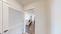Located at 2901 4th Ave S in Birmingham's Lakeview district, this three-bedroom residence at Lakeview Green delivers a clean, contemporary design across a single floor. The open-concept layout is anchored by a well-appointed kitchen featuring granite countertops, a center island with an undermount sink, light wood cabinetry, subway tile backsplash, stainless steel appliances including a gas range and refrigerator, and stylish pendant lighting — all set over rich hardwood-style flooring. A hallway with a louvered storage door connects the kitchen to the main living area, which is flooded with natural light through floor-to-ceiling windows and sliding glass doors that open to a private balcony overlooking the Birmingham cityscape. Built-in floating shelves add a functional design touch to the living space. Each bedroom features plush carpeting, ceiling fans, and windows with outdoor views. The primary bedroom includes a generous walk-in closet outfitted with wire shelving and coat hooks. The bathroom is finished with wood-look tile flooring, a soaking tub, and classic white subway tile surround. Throughout the residence, crisp white walls and recessed lighting contribute to a bright, modern ambiance.