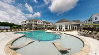 Located at 4115 Dr. Martin Luther King Jr. Blvd in New Bern, North Carolina, this two-story residential community offers a compelling blend of thoughtful architecture and resort-inspired amenities. The buildings feature a classic coastal aesthetic, characterized by gray lap siding, white trim, pitched rooflines, and private balconies that add both character and functionality to each level.

At the heart of the community lies an expansive, freeform swimming pool complex — a standout feature of the outdoor spaces. The pool area is generously sized with multiple entry points, in-water lounge chairs, and a broad surrounding deck furnished with chaise lounges, perfect for relaxing under the Carolina sun. A second, similarly styled pool adds to the resort-like atmosphere of the community.

A prominently positioned clubhouse, featuring large windows and a rounded architectural design, serves as a central gathering hub overlooking the pool deck. Additional outdoor amenities include a spacious patio area furnished with wicker seating arrangements, ideal for socializing, surrounded by manicured landscaping and decorative iron fencing. The grounds are well-maintained with lush greenery and thoughtfully placed lighting throughout. This community delivers a comprehensive outdoor living experience in a welcoming New Bern setting.