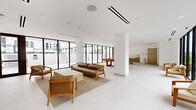 Located at 1155 NE 126th St in North Miami, FL, this contemporary amenity lounge is a generously proportioned, single-floor community space designed with a clean, modern aesthetic. The open-plan layout is anchored by expansive floor-to-ceiling windows framed in sleek black metal, flooding the interior with abundant natural light and offering views of the surrounding courtyard, outdoor stairways, and residential building facades.

The main living area features polished light-tiled flooring throughout and bright white walls that enhance the sense of openness and airiness. A seating arrangement of warm-toned wood-framed lounge chairs and a sofa is positioned atop a neutral area rug, creating an inviting social hub. A full-size pool table serves as a central recreational focal point, contributing to the space's lively, amenity-driven character.

Toward the rear of the space, a built-in kitchenette showcases warm wood cabinetry, a light stone countertop island, and a stainless appliance, ideal for hosting and gatherings. Recessed lighting and linear ceiling-mounted HVAC units maintain a refined, uncluttered overhead plane. Structural columns are integrated seamlessly into the layout. Large glass doors open directly to an outdoor terrace, reinforcing the indoor-outdoor connectivity that defines this bright, well-appointed North Miami community space.