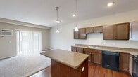 This one-bedroom, one-bathroom unit in Williston, North Dakota offers a practical and well-appointed layout across a single floor. The open-concept kitchen is a standout feature, boasting rich dark wood cabinetry, laminate countertops, a full suite of black appliances including a range, microwave, dishwasher, and refrigerator, and a central island with pendant lighting overhead. Warm hardwood-style flooring runs throughout the kitchen and living areas, creating a cohesive and inviting atmosphere. The living room flows naturally from the kitchen, offering sliding door access that brings in natural light. The bedroom is carpeted for comfort, featuring a large closet with bi-fold doors and a window that provides natural light. Neutral-toned walls throughout the unit lend a clean, move-in-ready aesthetic. The bathroom is efficiently designed with a full tub-shower combo, wood-toned vanity with a stone-look countertop, and hardwood-style flooring. A dedicated laundry area houses a full-size side-by-side washer and dryer with overhead wire shelving for added storage convenience. This unit delivers functional living with quality finishes in a compact, efficiently designed space.