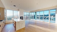 Located in the heart of Hollywood at 6390 De Longpre Ave, this single-floor high-rise residence offers a refined living experience defined by modern design and sweeping panoramic views of the Los Angeles cityscape and surrounding hills. The open-concept living and dining area is anchored by dramatic floor-to-ceiling glass walls on multiple sides, flooding the space with abundant natural light and framing breathtaking views at every turn. A sleek built-in fireplace adds a warm focal point to the living area, while light-toned hardwood flooring runs throughout the main living spaces, enhancing the bright and airy atmosphere. The gourmet kitchen is outfitted with light wood cabinetry, a tile backsplash, stainless steel appliances including a built-in oven and French door refrigerator, and a generously sized waterfall island topped with striking veined marble-look stone. The primary bathroom is a spa-inspired retreat featuring marble-tiled flooring, a freestanding soaking tub, a glass-enclosed walk-in shower with full-height tile surround, and a dual-sink vanity with a warm wood base beneath an elegant arched mirror. Bedrooms are carpeted and bright, with generous closet systems providing ample storage. A dedicated laundry area with side-by-side Bosch washer and dryer and overhead cabinetry adds everyday convenience to this thoughtfully designed residence.