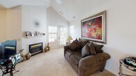 Located at 1990 Brandt Point Dr in Webster, NY, this single-floor home offers a well-organized layout with distinct living spaces designed for comfortable, everyday use. The living room serves as the focal point of the home, distinguished by soaring vaulted ceilings that lend a sense of openness and volume. A fireplace anchors one wall, while large windows and a glass door invite abundant natural light and provide views of the outdoors. Soft carpeting and neutral walls create a warm, inviting atmosphere throughout.

The dining area is positioned adjacent to the living space and features a glass-top table surrounded by upholstered chairs, illuminated by an elegant five-light chandelier overhead. Windows fitted with horizontal blinds allow natural light to filter in. A wooden hutch with glass displays adds classic warmth to the space.

The galley-style kitchen is efficiently arranged with warm oak cabinetry, light countertops, tile flooring, and standard appliances including a range and refrigerator. A louvered closet door provides additional pantry or storage access.

The bedroom is a comfortable, carpeted retreat with windows overlooking the surroundings, a wooden storage cabinet, and ample wall space. The bathroom features a wooden vanity with a single sink, lighted mirror, and tile flooring, offering a functional and tidy design.