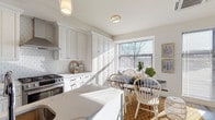 Located at 793 Post Rd E in Westport, Connecticut, this three-floor property offers a thoughtfully designed layout with contemporary finishes throughout. The kitchen serves as a centerpiece of the main living level, featuring white shaker cabinetry, a geometric tile backsplash, stainless steel appliances including a gas range with a wall-mounted hood, and a substantial island topped with striking marble-look quartz countertops. Pendant lighting illuminates the workspace, while a dedicated dining nook with a large window allows natural light to pour in. Light-toned hardwood flooring runs throughout the primary living areas, complementing the clean, neutral color palette.

The living area is bright and open, benefiting from floor-to-ceiling windows and sliding glass doors that connect directly to an outdoor balcony with views of the surrounding landscape. The bedrooms continue this indoor-outdoor connection, each offering balcony access through large sliding doors and closet storage. A clean, tile-floored full bathroom with white cabinetry provides functional convenience. A dedicated laundry area includes a stacked washer and dryer unit with built-in shelving. The lower level includes a spacious garage with concrete walls and additional unfinished storage space.