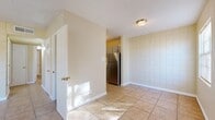 This single-floor space presents a cohesive and practical layout with a consistent design language throughout. A signature characteristic of the interior is the cream-colored, large-format grid-patterned wall paneling that appears across multiple rooms, lending a distinctive and uniform aesthetic to the space.

The kitchen is equipped with stainless steel appliances, including a full-size refrigerator and a gas range, set against tile floors and the same grid-patterned walls. An adjacent dining or flex area flows naturally from the kitchen, offering an open and functional transition between spaces.

The bedrooms are well-proportioned, each benefiting from natural light through window blinds and the same durable tile flooring found throughout. One bedroom features a ceiling fan for added comfort, while another includes a built-in closet with shelving, providing practical storage. A louvered-door closet adds additional storage options nearby.

The bathroom is outfitted with a full soaking tub and shower combination, accented by large-format earthy brown wall tiles that create a clean, cohesive look.

Throughout the space, white baseboards provide crisp contrast against the tile floors, and ceiling-mounted light fixtures ensure adequate illumination in every room. The overall ambiance is clean, neutral, and move-in ready.