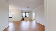 This 1-bedroom, 1-bathroom residence combines classic pre-war architectural character with functional, well-proportioned living spaces. Warm hardwood flooring flows consistently throughout the unit, creating a cohesive and inviting aesthetic from room to room.

The spacious living room is a standout feature, showcasing elegant wainscoting panels, crown molding, and a decorative ceiling medallion. A gold-toned chandelier adds a refined touch, while multiple windows invite generous natural light and offer views of the surrounding cityscape. A cast-iron radiator provides classic in-unit heating.

The kitchen is efficiently laid out with white cabinetry, granite-style countertops, a gas range, and full-size refrigerator. It opens conveniently toward the main living area, enhancing the sense of connectivity within the home.

The bedroom is a comfortable, well-sized retreat featuring a large closet with built-in shelving, a window with city views, and the same warm hardwood flooring found throughout. The wainscoting detailing continues here, maintaining the unit's cohesive architectural style.

The bathroom retains its classic pre-war charm with white hex tile flooring, full white subway tile walls with black accent trim, a pedestal sink, and a combined shower-tub. A connecting hallway with an additional window ties all rooms together seamlessly.