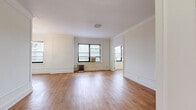 This 1-bedroom, 1-bathroom residence combines classic pre-war architectural character with functional, well-proportioned living spaces. Warm hardwood flooring flows consistently throughout the unit, creating a cohesive and inviting aesthetic from room to room.

The spacious living room is a standout feature, showcasing elegant wainscoting panels, crown molding, and a decorative ceiling medallion. A gold-toned chandelier adds a refined touch, while multiple windows invite generous natural light and offer views of the surrounding cityscape. A cast-iron radiator provides classic in-unit heating.

The kitchen is efficiently laid out with white cabinetry, granite-style countertops, a gas range, and full-size refrigerator. It opens conveniently toward the main living area, enhancing the sense of connectivity within the home.

The bedroom is a comfortable, well-sized retreat featuring a large closet with built-in shelving, a window with city views, and the same warm hardwood flooring found throughout. The wainscoting detailing continues here, maintaining the unit's cohesive architectural style.

The bathroom retains its classic pre-war charm with white hex tile flooring, full white subway tile walls with black accent trim, a pedestal sink, and a combined shower-tub. A connecting hallway with an additional window ties all rooms together seamlessly.