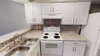Located at 2468 Laughlin Dr in Dallas, TX, this single-story home offers a well-designed layout with a mix of practical finishes throughout. The kitchen is a standout feature, showcasing crisp white cabinetry with brushed nickel hardware, light granite-style countertops, a stainless steel sink, and a mosaic tile backsplash in warm earth tones. A white electric coil range with an overhead ventilation hood completes the functional cooking space. The adjoining dining or utility area features wood-look laminate flooring that carries a warm, natural aesthetic. The living area is bright and open, with durable wood-look flooring, a textured ceiling, and a large window fitted with horizontal blinds that allow natural light to filter in. The bedrooms are finished with plush carpeting, ceiling fans, and windows with blinds, offering a comfortable and quiet retreat. One bedroom features two closets, adding notable storage capacity. The bathroom is well-appointed with a white vanity topped with a speckled countertop, a large mirror, wood-look flooring, and a tiled tub-and-shower combination accented with a decorative mosaic tile border and a built-in niche. The neutral color palette and textured ceilings throughout give the home a cohesive, move-in-ready feel.