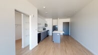 Located at 195 E Main St in the heart of downtown Columbus, Ohio, this modern single-floor unit offers a thoughtfully designed open-concept layout with clean lines and contemporary finishes throughout. Light wood-tone flooring runs continuously across the main living and kitchen areas, complementing the crisp white walls and creating a bright, cohesive aesthetic.

The kitchen is a standout feature, equipped with two-tone cabinetry — white upper cabinets paired with slate-blue lower cabinets — a white tile backsplash, a stainless steel sink, and black appliances including a range, microwave, and refrigerator. A central island with a white countertop provides additional prep space and serves as a natural divider between the kitchen and the open living area. Large windows in the living area invite generous natural light and offer views of the Columbus skyline, enhancing the urban feel of the space.

The bedroom is a well-proportioned, light-filled room with a window overlooking the cityscape and neutral walls that lend themselves to a variety of interior styles. Closet space is accessible nearby. The bathroom features a clean, all-white walk-in shower with a rainfall showerhead and built-in shelving niches, finished with polished chrome fixtures. The overall ambiance of the unit is modern, minimal, and well-suited for urban living.