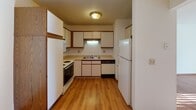 This single-floor unit offers a practical and well-organized layout with distinct living, kitchen, and bedroom areas. The living room is a bright, open space anchored by warm hardwood flooring that extends throughout the main areas. A full-width sliding glass door dressed with vertical blinds allows generous natural light to stream in, creating a sun-drenched atmosphere. Baseboard heaters and a wall-mounted air conditioning unit ensure year-round climate comfort. An adjoining area connects seamlessly to the rest of the unit, providing flexible use of space.

The kitchen is efficiently designed in a U-shaped configuration, featuring white cabinetry with wood-trimmed accents, light countertops, and a full suite of white appliances including a refrigerator, electric range, dishwasher, and microwave. A window above the sink adds ventilation and a touch of natural light to the cooking space, while hardwood flooring continues underfoot.

The bedrooms are carpeted for comfort and each include a ceiling fan with light fixture and a window with blinds. Baseboard heating keeps these rooms consistently warm. The bathroom is finished with hardwood flooring, a single-sink vanity with a light countertop, and a tub-shower combination, offering a clean and functional design throughout.