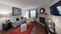 This single-floor residence offers a thoughtfully designed layout with distinct living, sleeping, and kitchen areas that flow naturally into one another. The living room serves as the heart of the home, centered around a tile-surround gas fireplace flanked by a decorative mirror. Natural light enters through a set of double windows and a glass door dressed with drape panels, illuminating the rich hardwood-style flooring beneath. A textured ceiling adds dimension to the space throughout.

The kitchen is efficiently arranged with warm oak cabinetry, granite-look countertops, and stainless steel appliances including a refrigerator, range, and microwave. A peninsula with bar seating and a skylight-style overhead fixture make this space both functional and inviting for casual dining.

The primary bedroom is generously proportioned, featuring plush carpeting, a ceiling fan with light fixture, and access to a walk-in closet with built-in shelving. An additional bedroom offers similar comfort with carpet flooring, a ceiling fan, and natural light from a side window.

The bathroom includes an oak vanity with a granite countertop, single-basin sink, and hardwood-style flooring, maintaining the cohesive material palette found throughout the home. Overall, the space presents a warm, practical, and comfortable environment.