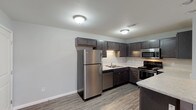 Unit 4621-D3 is a thoughtfully designed single-floor residence that combines modern finishes with a functional layout. The kitchen serves as a standout feature, showcasing dark espresso-toned shaker cabinetry, light marbled countertops, and a full suite of stainless steel appliances including a refrigerator, range, microwave, and dishwasher. A peninsula counter extends the workspace and provides an ideal spot for casual dining or meal prep. Wood-look plank flooring runs throughout the kitchen and entry areas, adding warmth and durability.

The open living area transitions seamlessly from the kitchen, with plush carpeting underfoot and a neutral gray color palette that lends a clean, contemporary feel. A dedicated entry door with adjacent recessed lighting welcomes residents into a generously sized main living space filled with natural light from a side window.

The bedroom is a comfortable retreat, featuring soft carpet, a ceiling light fixture, and direct access to both the bathroom and a spacious walk-in closet outfitted with wire shelving systems for organized storage. The bathroom is finished with wood-look flooring, dark vanity cabinetry, brushed nickel hardware, and a full soaking tub with a clean white surround. Throughout the unit, a consistent neutral tone and modern fixtures create a cohesive and inviting atmosphere.