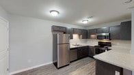 Unit 4621-D3 is a thoughtfully designed single-floor residence that combines modern finishes with a functional layout. The kitchen serves as a standout feature, showcasing dark espresso-toned shaker cabinetry, light marbled countertops, and a full suite of stainless steel appliances including a refrigerator, range, microwave, and dishwasher. A peninsula counter extends the workspace and provides an ideal spot for casual dining or meal prep. Wood-look plank flooring runs throughout the kitchen and entry areas, adding warmth and durability.

The open living area transitions seamlessly from the kitchen, with plush carpeting underfoot and a neutral gray color palette that lends a clean, contemporary feel. A dedicated entry door with adjacent recessed lighting welcomes residents into a generously sized main living space filled with natural light from a side window.

The bedroom is a comfortable retreat, featuring soft carpet, a ceiling light fixture, and direct access to both the bathroom and a spacious walk-in closet outfitted with wire shelving systems for organized storage. The bathroom is finished with wood-look flooring, dark vanity cabinetry, brushed nickel hardware, and a full soaking tub with a clean white surround. Throughout the unit, a consistent neutral tone and modern fixtures create a cohesive and inviting atmosphere.
