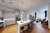 This well-appointed 4-bedroom, 4-bathroom single-story residence offers a thoughtfully designed layout that balances comfort and functionality. The open-concept kitchen and living area serves as the heart of the home, featuring sleek gray shaker cabinetry, white quartz countertops, stainless steel appliances, a large center island with an undermount sink, pendant lighting, and track lighting overhead. Warm hardwood flooring flows throughout the main living spaces, complemented by in-unit washer and dryer access. The living room is bright and inviting, centered around a ceiling fan with light fixture and floor-to-ceiling vertical blinds flanked by rich navy drapes, allowing for adjustable natural light. Each of the four bedrooms offers plush carpeting, generous closet space, and windows that bring in natural light. The primary bedroom is a comfortable retreat with direct access to its own bathroom. The four bathrooms maintain a clean, modern aesthetic with white subway tile surrounds, tub-shower combos, wood-tone flooring, and white vanities with ample storage. The overall ambiance of the residence is contemporary and cohesive, with crisp white walls and consistent finishes throughout that create a bright, welcoming atmosphere.