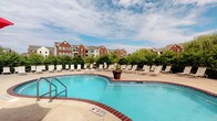 Located at 3280 Mill Run Dr in Hilliard, Ohio, this outdoor amenity space centers around a generously sized, curved swimming pool with crystal-clear blue water. The pool features a classic brick-trimmed surround and a gradual entry point, making it accessible and inviting. Surrounding the pool is a wide concrete sun deck lined with rows of lounge chairs, offering ample space for sunbathing and relaxation. A decorative planter with vibrant flowers serves as a charming focal point along the pool's edge, adding a touch of color to the space. The area is enclosed by lush, well-maintained shrubbery and fencing, providing a sense of privacy while maintaining an open, airy feel under open skies. In the background, the multi-story brick residential buildings with pitched rooflines and private balconies create an attractive architectural backdrop. The overall ambiance is one of a well-appointed community retreat, designed to offer residents a resort-like outdoor experience. The combination of thoughtful landscaping, comfortable amenities, and the picturesque surroundings makes this outdoor space a standout feature of the community.
