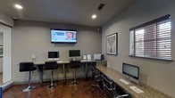 Located at 14402 W Bellfort St in Sugar Land, Texas, this single-floor dental office delivers a clean, modern environment designed to accommodate both staff efficiency and patient comfort. The space is thoughtfully organized to serve multiple functions seamlessly within one cohesive layout.

The reception and administrative area features an L-shaped granite countertop workstation equipped with multiple iMac computers, adjustable bar-height seating, a wall-mounted flat-screen television displaying dental service promotions, and a printer station — providing a fully functional hub for front-desk operations. Framed artwork adds a polished, professional touch to the neutral gray walls.

The patient waiting area offers a welcoming atmosphere with a pair of blue upholstered accent chairs accented with nailhead trim, arranged around a glass-top side table. Sliding glass panel partitions divide the space while maintaining an open, airy feel throughout. Recessed ceiling lighting illuminates the entire floor plan evenly.

Rich hardwood flooring flows through the primary areas, complemented by stone tile in transitional zones. Large windows allow natural light to filter into the space, enhancing the bright and professional ambiance. Archways and open corridors connect the various sections of the office, creating a smooth and intuitive flow from the entrance through to the clinical areas beyond.