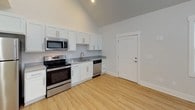This two-floor residence offers a well-designed layout with two bedrooms and two bathrooms, finished in a clean, contemporary style. The kitchen is a standout feature, boasting white shaker cabinetry, granite-style countertops, and a full suite of stainless steel appliances including a range, microwave, dishwasher, and refrigerator. Light wood-look flooring grounds the space and extends through the main living areas, complementing the bright, neutral walls and soaring vaulted ceilings that lend an airy, open feel.

The two bedrooms are carpeted for comfort and each include ceiling fans with lighting. One bedroom features a wall-mounted mini-split unit and a window that invites natural light, while the other opens directly to an en-suite bathroom. Both bathrooms are finished in crisp white tones. The primary bath includes a wide double-sink vanity with a large mirror, wood-look flooring, and a glass-enclosed shower. The secondary bath offers a tub-shower combination, single vanity, and a mirror with a natural light source nearby. The overall ambiance is modern, clean, and move-in ready.