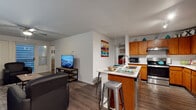 Located at 2704 Rio Grande St in Austin, TX, this single-story unit offers a well-designed, functional layout ideal for those seeking comfortable living near the University of Texas campus. The open-concept living and kitchen area forms the heart of the space, where warm wood-look flooring flows seamlessly throughout. The kitchen is equipped with stainless steel appliances — including a refrigerator, range, and dishwasher — rich wood cabinetry with ample storage, white countertops, and a central island with a double-basin sink and bar seating, perfect for casual dining or entertaining. The living room provides generous space for seating and features a ceiling fan, recessed lighting, and sliding glass doors that invite natural light. Multiple bedrooms offer comfortable accommodations, each with distinct character — one features a window with natural light and a built-in desk area, while others provide quiet retreats with clean, neutral walls. The bathrooms are finished with wood cabinetry, white countertops, and large mirrors; one features a double-sink vanity for added convenience. Wood-look flooring extends into the bathrooms, tying the design together cohesively. The overall aesthetic is clean, modern, and inviting throughout.