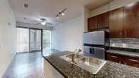 Located at 3616 Richmond Ave in Houston's Upper Kirby neighborhood, this well-appointed one-bedroom, one-bathroom residence offers a thoughtfully designed single-floor layout that maximizes every square foot. The open-concept living and kitchen area serves as the heart of the home, where rich hardwood flooring, a ceiling fan, and track lighting create a bright, welcoming atmosphere. Floor-to-ceiling sliding glass doors with vertical blinds flood the living space with natural light and provide access to an outdoor view. The kitchen is equipped with stainless steel appliances, including a refrigerator with ice maker, microwave, and range, complemented by dark granite countertops, a double stainless steel sink, and rich dark-wood cabinetry with a tile backsplash. The kitchen flows seamlessly into the living area via a peninsula counter. The hallway connects the living space to the private quarters, with convenient in-unit laundry — a full-size washer and dryer tucked neatly into a dedicated closet with shelving. The bedroom features plush carpeting, a ceiling fan, and a wide bank of windows offering neighborhood views. The bathroom is finished with tile flooring, a dark-wood vanity with granite countertop, and direct access to a carpeted walk-in closet complete with built-in shelving and hanging rods.