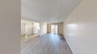 Located at 5160 Tamarus St in Las Vegas, NV, this one-bedroom, one-bathroom unit offers a well-organized single-floor layout across a comfortable footprint. The open living area features light gray wood-look flooring, neutral beige walls, and a textured ceiling, creating a clean and functional space. A sliding glass door fills the living room with natural light and provides access to a private balcony. The galley-style kitchen flows directly off the living area and is equipped with white cabinetry, dark granite-style countertops, white appliances including a refrigerator and electric range, and a window that brings in additional natural light. A hallway connects the main living spaces to the private areas of the unit. The bedroom is generously sized, featuring plush carpet, textured ceilings, and ample wall space, with direct access to a dedicated walk-in closet outfitted with built-in shelving and a hanging rod. The full bathroom includes a single-sink vanity with a dark countertop, a large mirror, a tub-shower combination, and wood-look flooring. Throughout the unit, the neutral color palette and practical finishes provide a versatile and move-in ready living environment.