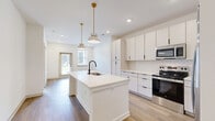 Located at 20 Graf Dairy Dr in Mobile, Alabama, this single-story, 3-bedroom, 2-bathroom home offers a clean, modern aesthetic defined by bright white walls, warm wood-look flooring, and thoughtfully selected finishes throughout. The open-concept kitchen and living area serves as the heart of the home, anchored by a large center island with a white quartz countertop, undermount sink, and stylish gold pendant lighting. The kitchen is fully equipped with stainless steel appliances, crisp white cabinetry, a herringbone tile backsplash, and abundant storage. The living area flows seamlessly from the kitchen, with access to a rear door that brings in natural light. The primary bedroom features plush carpeting, a ceiling fan, and a dedicated en-suite bathroom complete with warm wood vanity cabinetry, a white quartz countertop, dual sinks with matte black fixtures, and a framed mirror with gold accent lighting. A walk-in closet is also accessible from the primary bath. The additional bedrooms offer carpeted or hardwood-style flooring, multiple windows, and ceiling fans for comfort. A dedicated laundry area and five closets throughout the home provide generous storage. The single-story layout ensures effortless accessibility and functionality throughout.
