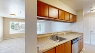 This single-floor residential unit offers a thoughtfully designed layout that balances functionality and comfort. The kitchen is a standout feature, equipped with warm medium-tone wood cabinetry, granite-style countertops, stainless steel appliances including a refrigerator, range, microwave, and dishwasher, and a stainless steel sink. A galley-style configuration maximizes workspace efficiency, while a breakfast bar peninsula opens directly to the living area, creating a seamless open-concept flow. The living room is generously proportioned, finished with plush neutral carpeting, and features large sliding glass doors and additional windows that invite an abundance of natural light and views of surrounding greenery. The bedrooms are well-sized, carpeted for comfort, and include access to closets, with windows framing outdoor foliage. The bathrooms are clean and functional, featuring wood-tone vanities with light countertops, a tub-shower combo, and wood-look tile flooring. One bathroom includes accessibility grab bars. Warm beige tones carry throughout the unit, creating a cohesive and neutral palette. The textured ceilings and clean white trim add a classic finishing touch to this practical and comfortable single-level residence.