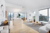 This single-floor residence is designed with a cohesive minimalist aesthetic, combining clean white walls, wide-plank light hardwood flooring, and floor-to-ceiling windows that frame sweeping views of both the waterfront and city skyline. The open-concept living and dining area is anchored by generous windows on multiple sides, bathing the space in natural light and providing an ever-present connection to the urban and aquatic landscape beyond.

The living room offers a serene, neutral palette with a plush sectional sofa, a round rattan coffee table, and a large gold-framed oval mirror that reflects the water views. Adjacent, the dining area features cane-back chairs around a natural wood table, positioned to take full advantage of the skyline panorama.

The kitchen is thoughtfully designed with flat-front, light wood cabinetry extending to the ceiling, integrated appliances, a sleek induction cooktop, and a substantial waterfall-edge island with bar seating. Bold abstract artwork punctuates the transition between kitchen and living spaces.

The primary bathroom is spa-like, featuring large-format neutral stone tiles, a freestanding soaking tub, a glass-enclosed shower, and a floating wood vanity. Bedrooms are bright and airy, each benefiting from expansive city or water views. A dedicated study nook with waterfront views and a well-connected hallway complete the thoughtfully arranged layout.