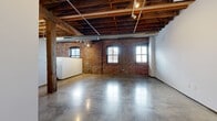 Located in St. Louis's vibrant Washington Avenue corridor, this single-floor loft space masterfully blends industrial heritage with modern functionality. The main open area commands attention with its dramatic exposed timber beam ceiling, original structural wood columns, and fully visible ductwork that celebrate the building's historic character. Warm red brick walls line the perimeter, punctuated by large arched and multi-pane windows that invite generous natural light and lend an airy, open ambiance to the space. Polished concrete floors run throughout, reflecting light and adding a sleek, contemporary contrast to the raw industrial elements above. Track lighting mounted to the ceiling beams provides flexible, directed illumination across the open floor plan. A well-equipped kitchen features light maple cabinetry, stainless steel appliances including a refrigerator, range, over-the-range microwave, and dishwasher, along with ample counter and storage space. Freestanding white partition walls within the open plan offer versatile options for defining functional zones without disrupting the loft's expansive feel. A bathroom provides essential amenities, highlighted by a polished chrome heated towel rack and concrete flooring consistent with the rest of the space. This distinctive loft offers a compelling combination of historic architectural detail and modern convenience.