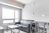 Located at 275 Larch Street in Waterloo, Ontario, this 2-bedroom, 1-bathroom unit offers a thoughtfully organized layout across a single floor. The space is designed for efficient living, with each room serving a clear functional purpose.

The kitchen is outfitted with contemporary dark wood-grain cabinetry extending to the ceiling, a stone-look countertop, a double stainless steel sink, a subway tile backsplash, and stainless steel appliances including an electric range and dishwasher. Light wood-style flooring runs throughout, contributing to a clean, modern aesthetic.

The bedrooms are bright and simply finished with neutral walls. The primary bedroom features large windows alongside a sliding glass door that opens to a balcony, offering views of the surrounding Waterloo streetscape and green space. Natural light flows generously into the room. The second bedroom is comparably appointed and compact in scale.

The bathroom includes a full soaker tub and shower combination with a white acrylic surround featuring built-in corner shelving, complemented by classic tile flooring.

A utility area with a wall-mounted electrical panel and ceiling-integrated HVAC unit keeps essential building systems accessible. Overall, the unit presents a clean, modern interior well-suited for functional day-to-day living in a central Waterloo location.