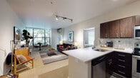 Located in Portland's vibrant Pearl District, this thoughtfully designed single-floor residence offers a seamless open-concept layout that connects the kitchen, dining, and living areas into one cohesive living space. The kitchen is a standout feature, outfitted with rich dark wood cabinetry, stainless steel appliances including a range, microwave, and refrigerator, a classic white subway tile backsplash, and a quartz-topped peninsula with an undermount sink — ideal for both cooking and casual entertaining. The living area is bright and welcoming, featuring carpet flooring, a wall-mounted split unit for climate control, and track lighting overhead. A glazed corner window floods the dining nook with natural light and frames leafy outdoor views, creating a serene setting for everyday meals. The bedroom is generously proportioned with plush carpet, a large window overlooking greenery, and access to a walk-in closet. Two full bathrooms are finished with wood-look vinyl flooring, quartz countertops, and tub/shower combinations. Throughout the residence, neutral tones and clean lines create a calm, contemporary ambiance well-suited to urban living in one of Portland's most walkable and dynamic neighborhoods.
