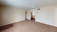 This single-story residence offers a practical and functional layout across several well-defined spaces. The living area serves as the main gathering space, featuring warm beige walls, plush wall-to-wall carpeting, and a window that allows natural light to fill the room. An entryway with wood-look flooring transitions into the carpeted interior, providing a clear delineation at the front door.

The kitchen is designed for efficiency, featuring a galley-style layout with white cabinetry, yellow-toned countertops, and wood-look flooring. Appliances include a stainless steel gas range with overhead ventilation, a white refrigerator, and a dishwasher. A recessed ceiling light fixture illuminates the workspace effectively.

Two bedrooms share a consistent design, each offering plush carpeting, beige walls, and ceiling fans with integrated light fixtures. Windows in each room provide natural light and ventilation.

Two bathrooms serve the residence, each equipped with a full-size soaking tub and shower combination with white square tile surrounds and chrome fixtures. One bathroom includes a window for added natural light and ventilation. Both bathrooms maintain a clean, straightforward design consistent with the overall aesthetic of the home.