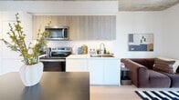 Located on the 16th floor of a modern Toronto high-rise at 748 Bathurst Street, this two-bedroom, one-bathroom unit offers an efficient and well-designed layout across a compact single floor. The unit's most distinctive architectural feature is its exposed concrete ceiling with visible ductwork, lending an industrial-loft aesthetic that contrasts effectively with the otherwise bright, white interior finishes and light wood flooring throughout.

The open-concept kitchen is outfitted with two-tone cabinetry — combining light wood uppers with white lower cabinets — white quartz countertops, and stainless steel Whirlpool appliances including a range, over-the-range microwave, and undermount sink. The kitchen flows seamlessly into the living area, making the space feel cohesive and functional.

The primary bedroom benefits from floor-to-ceiling windows on two walls, framing expansive panoramic views of the Toronto skyline and surrounding neighbourhood, with a concrete column adding to the industrial character. The second bedroom is more intimate in scale, featuring a large window with wide city views and the same exposed concrete ceiling detail.

The bathroom is clean and functional, featuring a full soaker tub with shower, white tile surround, and a simple, well-maintained design. A private balcony extends the living space outdoors, offering elevated views across the cityscape.