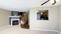 This two-story residence offers a well-organized layout designed for comfortable everyday living. The main floor centers around an open living area finished with plush carpeting and a ceiling fan overhead. A striking fireplace with a white mantle and dark gray accent wall serves as the focal point of the living room, adding both warmth and visual interest to the space. A smooth transition from carpet to rich dark hardwood flooring guides the eye toward the staircase, which features warm wood banisters and leads to the upper level. The open-concept design connects the living area to the kitchen through a convenient pass-through window, allowing for easy interaction between the two spaces. The kitchen is appointed with medium-toned wood cabinetry, dark countertops, and black appliances, with a pendant light adding a touch of character above. A textured ceiling runs throughout the main floor, contributing to the home's traditional aesthetic. The staircase is centrally positioned, making the upper floor easily accessible. Together, the thoughtful layout, warm finishes, and functional flow make this a practical and inviting home suited for a variety of lifestyles.