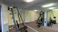 Located at 4051 E Olive Rd in Pensacola, Florida, this single-floor fitness center is designed to support a well-rounded exercise routine. The space is equipped with multi-station strength training machines, providing users with a variety of resistance and weight-based workout options. Floor-to-ceiling wall mirrors span a generous portion of the room, enhancing the sense of space while allowing users to monitor their form during exercise. The carpeted flooring adds a layer of comfort underfoot and helps define the workout area. Walls are finished in a neutral warm tone, contributing to a clean and focused atmosphere. Overhead flush-mount lighting ensures the space is consistently and evenly illuminated throughout. A textured ceiling completes the functional interior. Ventilation is supported by visible ceiling vents, maintaining a comfortable environment during use. The layout is open and practical, allowing for easy movement between equipment. Overall, this fitness center offers a well-appointed and functional environment suited for strength training and general fitness activities.