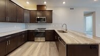 This single-floor unit showcases a contemporary design with a cohesive palette of warm neutrals and rich dark finishes throughout. The kitchen is a standout feature, equipped with dark espresso shaker-style cabinetry, granite countertops, a herringbone tile backsplash, and a full suite of stainless steel appliances including a range, over-the-range microwave, refrigerator, and dishwasher. Light-toned luxury vinyl plank flooring flows seamlessly through the living areas, complementing the neutral-toned walls and clean white trim.

The living and dining areas are generously proportioned, offering an open feel with recessed and flush-mount lighting. Multiple windows and glass doors provide natural light and balcony access, with views of surrounding trees and the outdoors.

The bedrooms are bright and well-sized, with windows framing exterior views and ample wall space. A large primary bedroom includes a ceiling fan and direct access to a private balcony.

Two bathrooms are finished to a high standard. The primary bath features a walk-in shower clad in marble-style tile, a dual-sink vanity with granite counters, and large-format marble tile flooring. The second bath offers a tiled tub-shower combination and matching marble-look flooring.