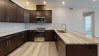 This single-floor unit showcases a contemporary design with a cohesive palette of warm neutrals and rich dark finishes throughout. The kitchen is a standout feature, equipped with dark espresso shaker-style cabinetry, granite countertops, a herringbone tile backsplash, and a full suite of stainless steel appliances including a range, over-the-range microwave, refrigerator, and dishwasher. Light-toned luxury vinyl plank flooring flows seamlessly through the living areas, complementing the neutral-toned walls and clean white trim.

The living and dining areas are generously proportioned, offering an open feel with recessed and flush-mount lighting. Multiple windows and glass doors provide natural light and balcony access, with views of surrounding trees and the outdoors.

The bedrooms are bright and well-sized, with windows framing exterior views and ample wall space. A large primary bedroom includes a ceiling fan and direct access to a private balcony.

Two bathrooms are finished to a high standard. The primary bath features a walk-in shower clad in marble-style tile, a dual-sink vanity with granite counters, and large-format marble tile flooring. The second bath offers a tiled tub-shower combination and matching marble-look flooring.