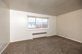 Located at 4925 Franklin Ave in Des Moines, Iowa, this single-floor unit offers three bedrooms, one bathroom, a living room, kitchen, and hallway. Throughout the space, neutral carpet flooring, white walls, and radiator heating units create a consistent, functional aesthetic.

The living room is bright and open, featuring a large multi-pane window that brings in natural light and views of the surrounding neighborhood. The bedrooms are similarly carpeted, each offering generous windows with radiator heaters beneath. Several bedrooms include ceiling fans, and at least one features a built-in closet with a hanging rod. An arched hallway detail connects the rooms, adding a subtle architectural touch.

The kitchen stands out with granite-look countertops, white cabinetry, a classic white subway tile backsplash, a stainless steel double sink, and tile flooring. A large window over the counter fills the space with natural light.

The bathroom retains its vintage character with salmon-pink ceramic wall tiles, black accent trim, mosaic tile flooring, and a window for ventilation. A shower-tub combo with a decorative curtain completes the room.

Overall, the unit offers a straightforward, livable layout with classic details and practical features throughout.
