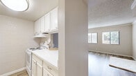 Located at 8429 N 27th Ave in Phoenix, Arizona, this one-bedroom, one-bathroom unit offers a well-organized single-floor layout designed to maximize every square foot of its cozy footprint. The living room greets you with warm wood-look flooring, neutral-toned painted brick walls, a textured ceiling, and a pair of windows fitted with blinds that invite natural light while maintaining privacy. A pass-through window connects the living area to the kitchen, enhancing the open feel between the two spaces. The kitchen features white cabinetry visible through the pass-through, offering a clean and functional workspace. The bedroom is a comfortable size, appointed with the same wood-look flooring, a painted brick accent wall, a textured ceiling, and a window overlooking greenery outside — providing a calm, naturally lit retreat. The hallway leads to a neatly appointed full bathroom, complete with a white vanity with drawer storage, wood-look tile flooring, and a tub/shower combination accented by elegant marble-style tile surround. A standout feature is the in-unit stacked washer and dryer, tucked conveniently into a dedicated alcove off the hallway, adding exceptional practicality to this efficiently designed home.