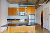 Located at 1425 P St NW in Washington, DC's vibrant Logan Circle neighborhood, this loft-style unit delivers an industrial-modern aesthetic across a well-appointed single-floor layout with 1 bedroom, 2 bathrooms, and a dedicated office. The open-plan living, dining, and kitchen area anchors the space, showcasing signature industrial details including exposed concrete ceilings with visible ductwork, polished terrazzo-style flooring, and exposed concrete structural columns that add architectural character throughout. Large, floor-to-ceiling windows flood the living area with natural light while offering city views of the surrounding DC streetscape, creating a bright and airy atmosphere. The kitchen is outfitted with warm wood cabinetry, dark granite countertops, stainless steel appliances, and a central island that doubles as a breakfast bar. Two bathrooms include a full bath with tile surround and shower, and a compact half bath with pedestal sink. The private bedroom features carpeted flooring and access to natural light, while the separate office provides a quiet, carpet-floored workspace. Two closets and an in-unit laundry room complete the thoughtfully organized layout, making this an efficiently designed urban residence in the heart of DC.