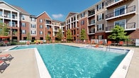 Located at 5541 Bowland Pl in Dublin, Ohio, this residential community combines classic architectural character with modern amenity-driven living. The exterior showcases attractive multi-story buildings clad in rich red brick and complementary neutral siding, with dark-shuttered windows that lend a traditional, polished appearance throughout the complex.

A standout feature of the community is its expansive outdoor swimming pool, which serves as a central gathering space for residents. The pool area is generously sized, with clear blue water surrounded by a well-maintained pool deck furnished with lounge chairs and shade umbrellas, creating an inviting retreat for relaxation and recreation. The deck is enclosed by a secure fence, offering both safety and a sense of privacy.

The surrounding buildings feature private balconies and covered terraces that overlook the pool courtyard, allowing residents to enjoy outdoor views from the comfort of their own homes. Mature trees interspersed throughout the grounds soften the built environment and contribute to a welcoming, landscaped atmosphere.

Situated in the desirable Dublin, Ohio area, the community benefits from a well-planned suburban setting known for its quality of life, strong local amenities, and easy access to major thoroughfares. The combination of classic design, thoughtful landscaping, and resort-style outdoor amenities makes this a distinctive and comfortable place to call home.