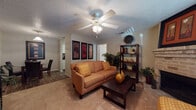This single-floor residence offers a thoughtfully laid-out living space designed for comfort and functionality. The living room serves as the heart of the home, featuring warm carpeted flooring, a textured ceiling, and a ceiling fan with integrated lighting. A standout brick fireplace anchors one wall, adding a classic, cozy element to the space. Framed artwork and open shelving provide decorative character, while windows with blinds allow for natural light throughout.

The galley-style kitchen is efficiently designed with white cabinetry, dark granite-style countertops, and wood-look flooring. Black appliances, including a refrigerator, electric range, microwave, and dishwasher, are neatly arranged along both sides, maximizing workspace and storage.

The bedroom is generously proportioned with plush carpet, natural light from a window with blinds, and direct access to both a walk-in closet and an en-suite bathroom. The bathroom is equipped with a tub-shower combination. Decorative wall panels in the bedroom add a refined touch to the overall aesthetic.

Throughout the residence, neutral tones and warm earth-colored accents create a cohesive and inviting atmosphere, making this a comfortable and practical living space.