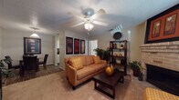 This single-floor residence offers a thoughtfully laid-out living space designed for comfort and functionality. The living room serves as the heart of the home, featuring warm carpeted flooring, a textured ceiling, and a ceiling fan with integrated lighting. A standout brick fireplace anchors one wall, adding a classic, cozy element to the space. Framed artwork and open shelving provide decorative character, while windows with blinds allow for natural light throughout.

The galley-style kitchen is efficiently designed with white cabinetry, dark granite-style countertops, and wood-look flooring. Black appliances, including a refrigerator, electric range, microwave, and dishwasher, are neatly arranged along both sides, maximizing workspace and storage.

The bedroom is generously proportioned with plush carpet, natural light from a window with blinds, and direct access to both a walk-in closet and an en-suite bathroom. The bathroom is equipped with a tub-shower combination. Decorative wall panels in the bedroom add a refined touch to the overall aesthetic.

Throughout the residence, neutral tones and warm earth-colored accents create a cohesive and inviting atmosphere, making this a comfortable and practical living space.